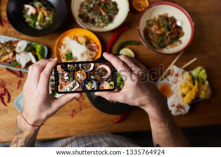 Above view closeup of unrecognizable man taking picture of Asian food dishes, copy space
