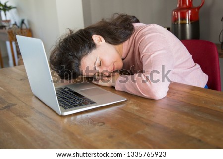 Young woman tired form work at laptop leaning on table. Freelance lady in casual sweater napping during day. Sleeping in home office concept 