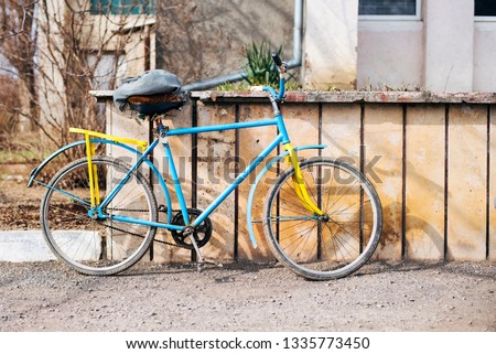 An old bike on which the grandfather goes to work. The bike is blue yellow without a lock standing on the street so that it is easy to steal