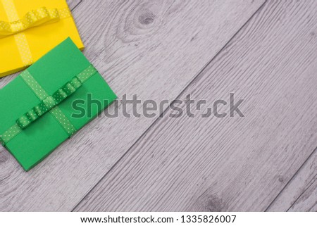 Hands holding craft paper green and yellow gift boxes with as a present for Christmas, new year, valentine day, mothers day and womans day or anniversary on wooden background.