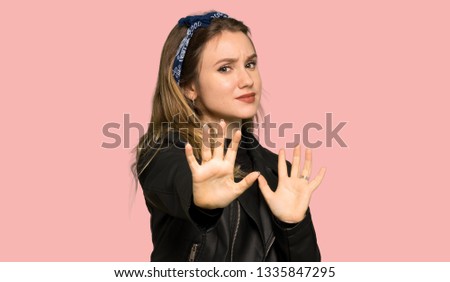 Teenager girl with leather jacket is a little bit nervous and scared stretching hands to the front on isolated pink background