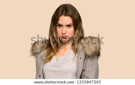 Teenager girl with coat with sad and depressed expression on isolated yellow background