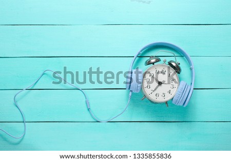 Vintage alarm clock with headphones on wooden background. Top view, minimalism