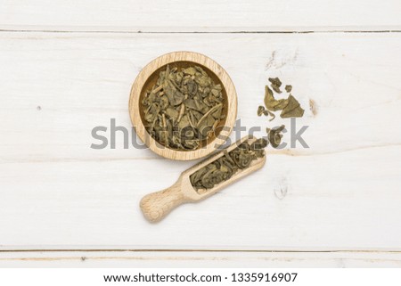 Lot of pieces of dry green tea in a scoop with wooden bowl flatlay on white wood