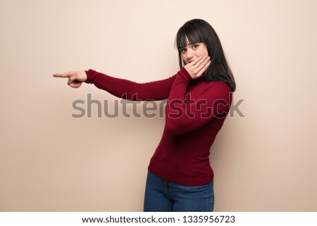 Young woman with red turtleneck pointing finger to the side with a surprised face
