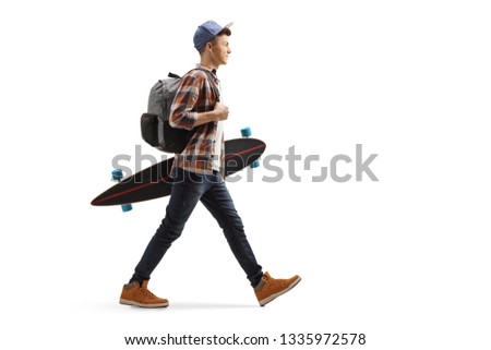 Full length profile shot of a male student walking and holding a longboard isolated on white background
