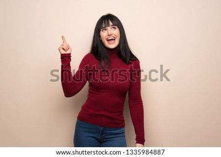 Young woman with red turtleneck intending to realizes the solution while lifting a finger up