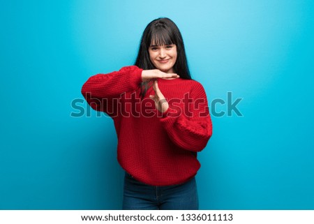 Woman with red sweater over blue wall making time out gesture