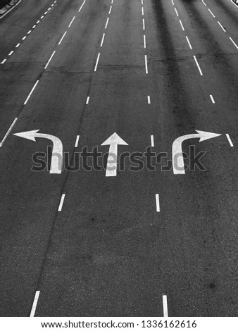 Arrow directions on asphalt road at a junction in black and white (monochrome).