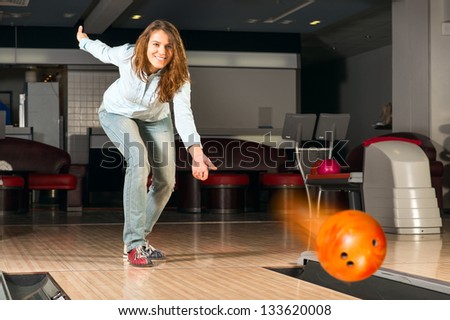 pleasant young woman throws a bowling ball, looks at the target and smiling