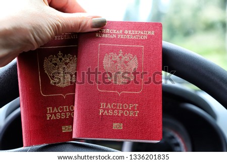 Russian passports in the hand of woman and and the steering wheel of a car with a blurred road and landscape in the background. Concept of travel abroad by car for Russian citizens
