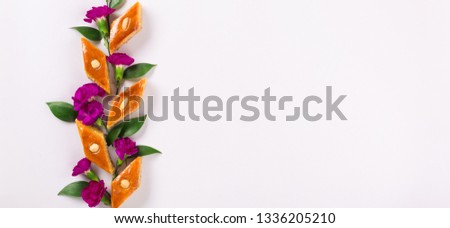 Novruz floral composition of traditional Azerbaijan pastry pakhlava or bakhlava, violet flowers and green leaves for spring celebration, light lilac oriental pattern background, top view, copy space 