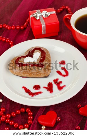 Chocolate cookie in form of heart with cup of coffee on pink tablecloth close-up