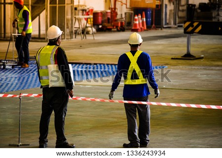Worker stretching the red white warning tape to the pole at construction site.Red and white Hazardous restricted area tape at construction area of factory to mark territory works.