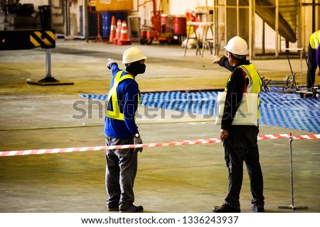 Worker stretching the red white warning tape to the pole at construction site.Red and white Hazardous restricted area tape at construction area of factory to mark territory works. Royalty-Free Stock Photo #1336243937