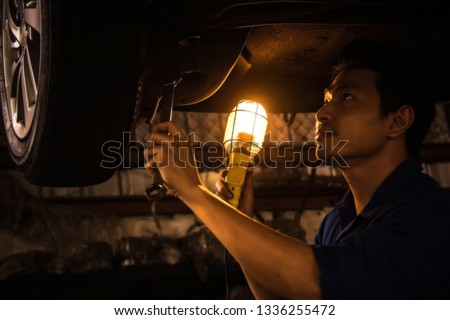 Car service concept : The mechanic examines the rear wheel of the car, using a wrench to fix the defect while repairing the suspension system for safety and overtime. Use a visual aid lamp.
