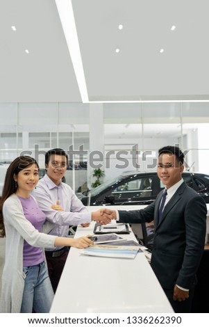 Happy family of two shaking hands of dealership manager and signing contract after buying new car