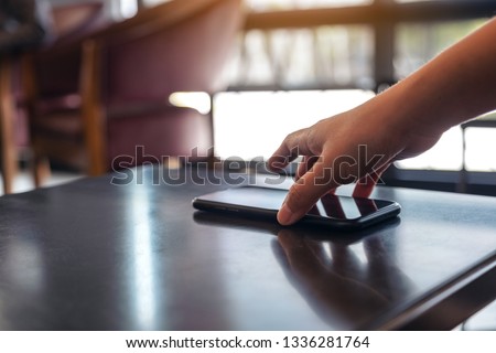 A hand grabbing and picking up mobile phone on the table  Royalty-Free Stock Photo #1336281764