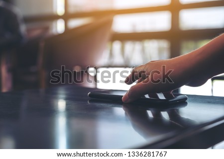 A hand grabbing and picking up mobile phone on the table  Royalty-Free Stock Photo #1336281767
