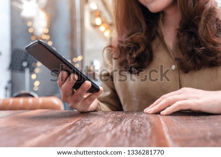 Closeup image of a beautiful woman holding , using and looking at smart phone in cafe