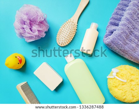 Flat lay still life photography bath products. Purple, yellow sponges, cotton towel, soap bar, shampoo, hair balm, wooden comb and rubber duck on a blue background