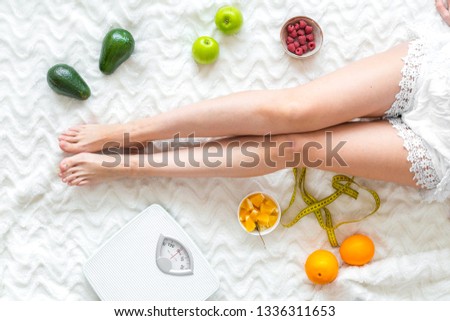 Girl on bed background top view with fruit for fitness breakfast, measuring tape and scale Royalty-Free Stock Photo #1336311653