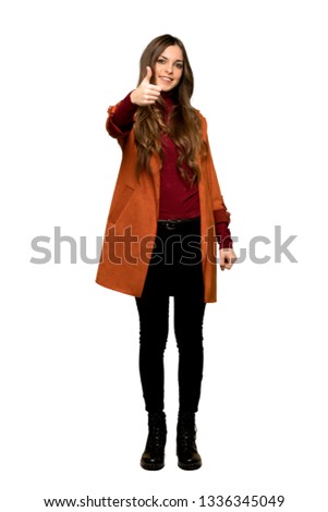 Full-length shot of Young woman with coat giving a thumbs up gesture because something good has happened on isolated white background