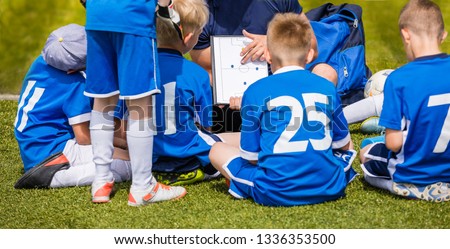 Coach Coaching Kids Soccer Team. Youth Football Team with Coach at the Soccer Stadium. Boys Listening to Coach's Instructions Before Competition. Coach Giving Team Talk Using Soccer Tactics Board
