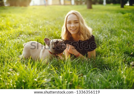A beautiful blonde sitting on the grass in a park with a small pug