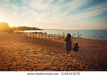 Beautiful mother and her little daughter are having fun together on the lake Ladoga in Russia during the sunset. Image with selective focus, noise effects and toning.