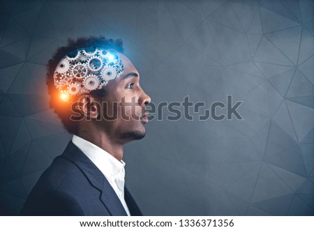 Side view of serous young African American businessman in suit with gear brain inside his head. Geometric pattern wall background. Mock up Royalty-Free Stock Photo #1336371356