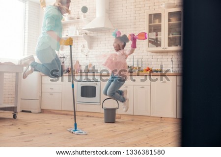 Jumping high. Mother and daughter wearing jeans jumping high after finishing the cleaning of apartment