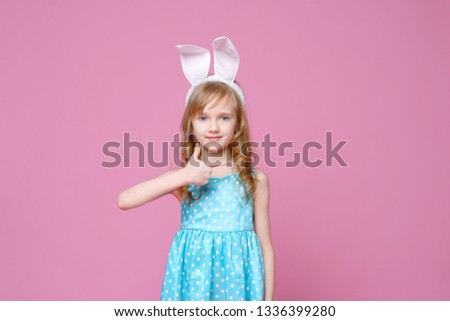 Cute blonde in the shape of an Easter Bunny and a blue dress with a pea pattern pointing her finger to the side. Concept of a holiday, advertising and fashion. happy Easter. Selective focus.