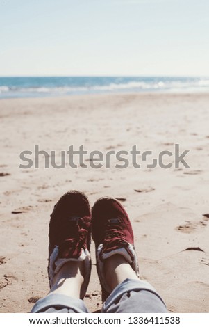 Feet of young woman in sport footwear and jeans relaxing after hiking on sand beach. POV. Adventure concept backdrop for motivational quotes, blog posts, your text. Toned image