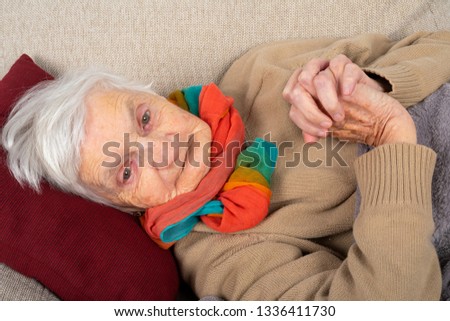 Close up picture of a sick old lady lying on the couch wrapped in a blanket, wearing colorful scarf