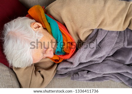 Close up picture of a sick old lady lying on the couch wrapped in a blanket, wearing colorful scarf