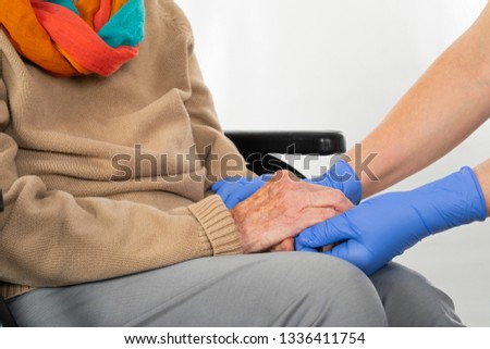 Close up picture of medical nurse wearing blue sterile gloves holding old disabled woman's hands