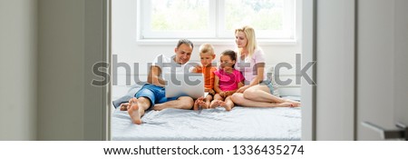 Portrait of Asian family looking at a tablet computer while lying on the bed, little asian girl using laptop with her parents. Weekend holiday leisure time education concept
