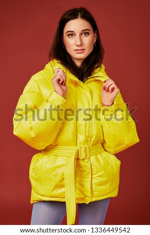 Studio portrait of young brunette woman in yellow down jacket and grey blue panty hoses or stockings. Studio shot
