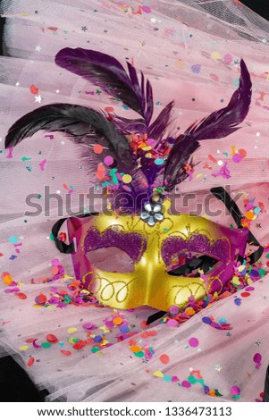 Carnival mask with feathers and confetti on pink tulle fabric and black background