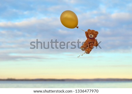  Bear toy flying to the sky with a yellow balloon.  Bear in the sky over the lake.                            