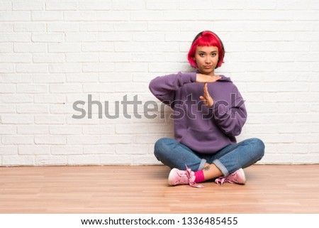 Young woman with pink hair sitting on the floor making time out gesture