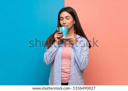 Young woman over pink and blue wall holding a hot cup of coffee