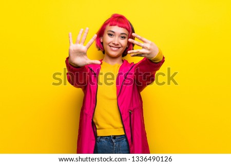Young woman with pink hair over yellow wall counting nine with fingers