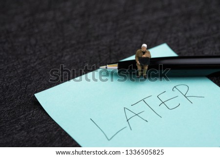 Miniature businessman sitting on pen and sticky note with hand writing the word Later on dark black background using as procrastination, lazy and postpone concept. Royalty-Free Stock Photo #1336505825