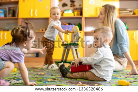 Nursery babies with mentor playing in kindergarten Royalty-Free Stock Photo #1336520486