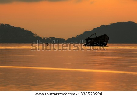 photographer taking a photo of wreck boat on shallow sea beach against beautiful sun rising sky