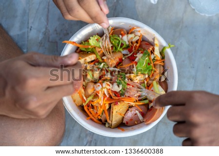 Three male hands with forks eat thai vegetable salad along with sausages, top view, closeup. Thailand