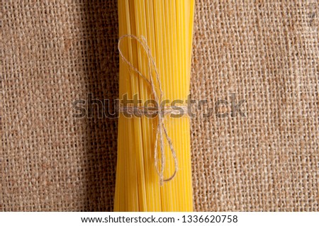 Bunch of raw spaghetti, tied with rope on sackcloth. In the center of the picture. Top view.