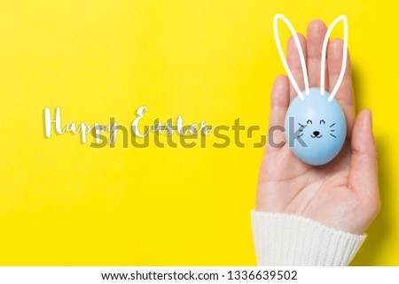 hand holding colorful pastel easter eggs on yellow background, happy easter concept